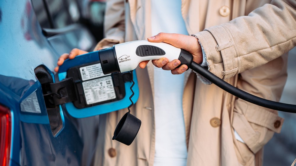 Eine Person steckt ein Ladekabel in ein blaues Elektroauto, um es aufzuladen.